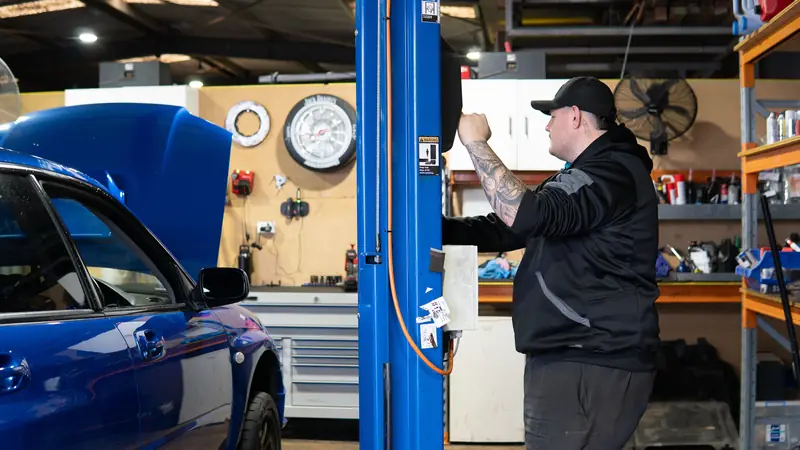 Riley Matthews at the hoist next to a blue WRX STI in the RJM workshop