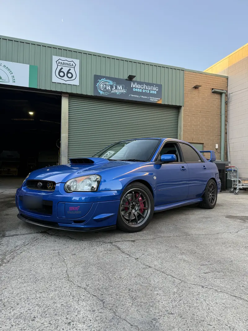Blue bug-eye WRX STI in front of the RJM Performance workshop and sign