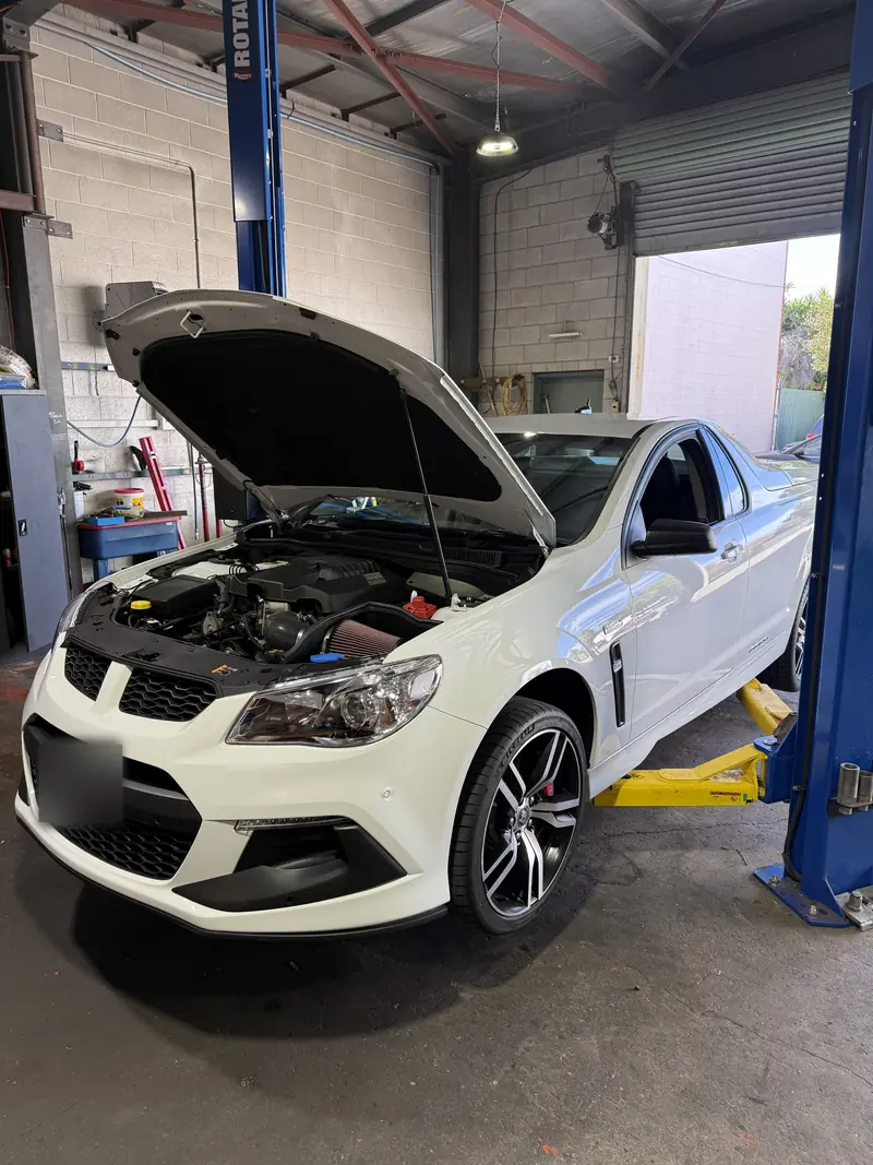 White V8 ute on the hoist in the RJM workshop with the bonnet up