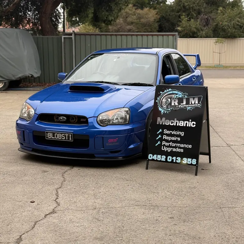 Blue bug-eye Subaru WRX STI parked next to the RJM Performance A-frame sign