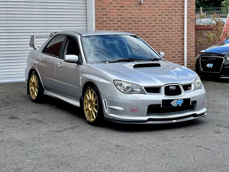 Silver hawkeye Subaru WRX STI with gold wheels parked by a brick building